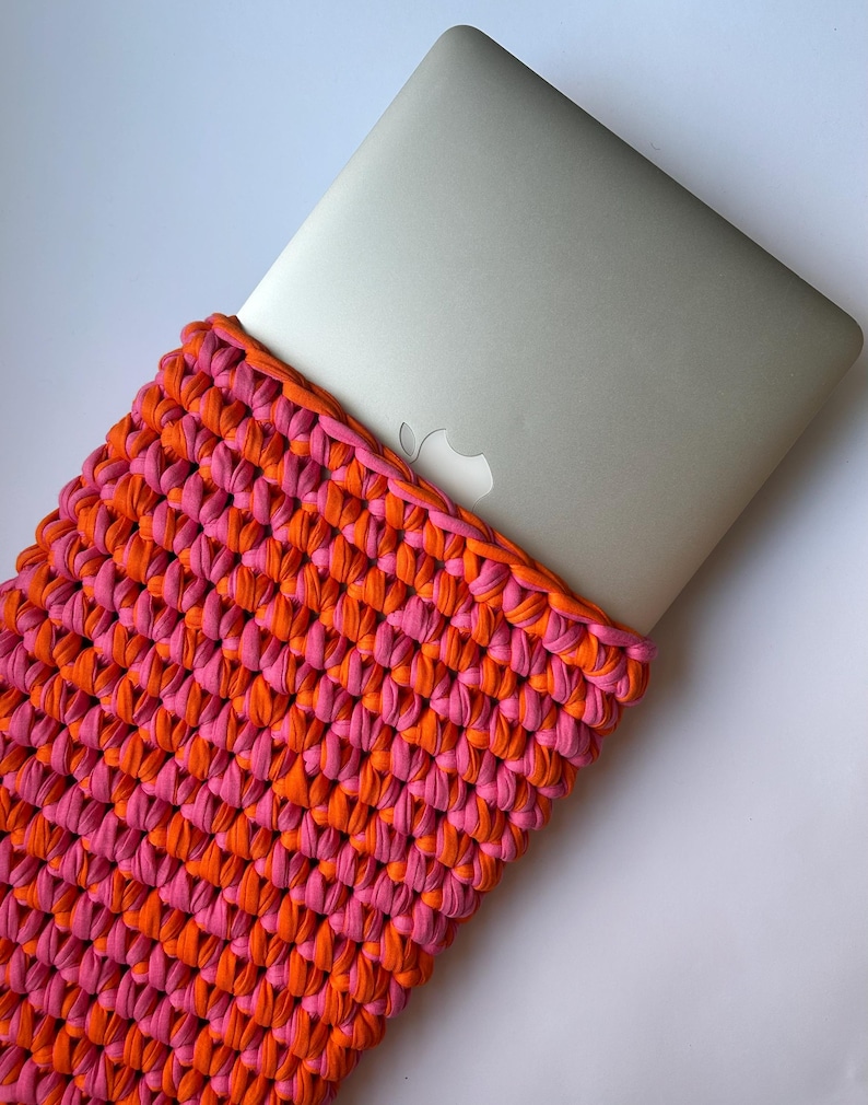 May include: A pink and orange crocheted laptop sleeve. The sleeve is made of thick yarn and has a simple, modern design.