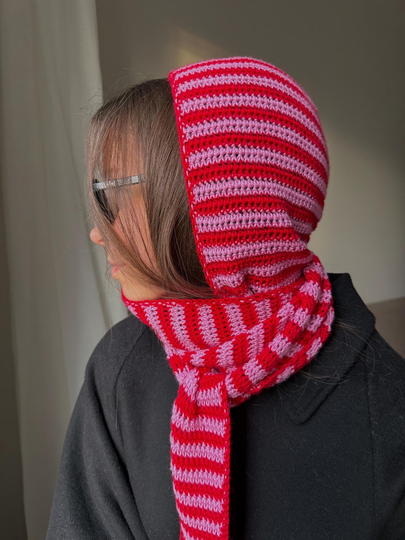 Puede incluir: Conjunto de capucha y bufanda de ganchillo a rayas rojas y rosas. La capucha presenta rayas horizontales, mientras que la bufanda tiene un dise&ntilde;o de tablero de ajedrez. El conjunto est&aacute; hecho de un hilo suave y texturizado, ideal para cualquier atuendo.