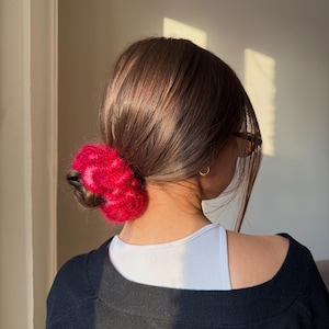 May include: A bright red and pink fluffy hair claw clip. The clip is made of a soft, textured material and is styled in the hair. The hair accessory is a stylish addition to any hairstyle.