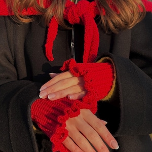 May include: A black coat with a red crocheted scarf and matching wrist warmers. The wrist warmers have a ruffled edge. The scarf is tied in a bow. The coat has a zipper closure.
