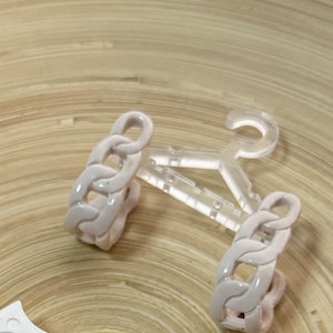 May include: A white plastic hanger with a chain link design on the ends. The hanger is designed to hold small items like jewelry or accessories.