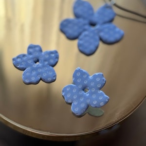 May include: Three blue ceramic flower charms with white polka dots. The charms are in the shape of a five-petal flower.