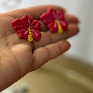 May include: Two red hibiscus flower shaped earrings with yellow centers.