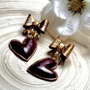 May include: A pair of earrings with a gold bow and a dark red heart pendant.