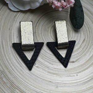 May include: A pair of black triangle shaped earrings with gold glitter rectangles in the center.