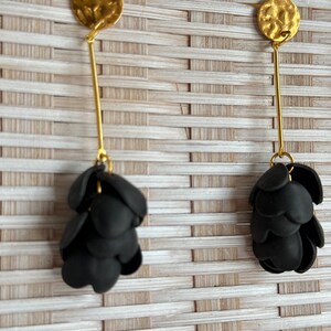 May include: A pair of gold dangle earrings with black flower-shaped charms. The earrings have a hammered gold disc at the top and a long, thin gold wire that connects to the charms.