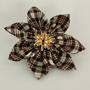 Puede incluir: Una flor de tela a cuadros marrones y blancos con un acento de hoja marrón y amarilla en el centro.