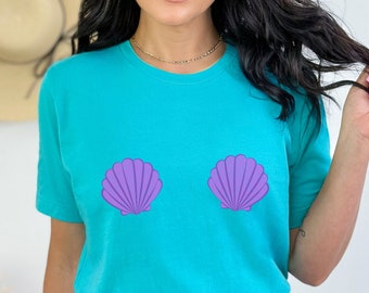 May include: A turquoise blue t-shirt with two purple seashells printed on the front. The shells are positioned on the chest area.