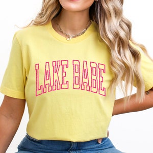 May include: A yellow t-shirt with the text "LAKE BABE" in pink lettering.