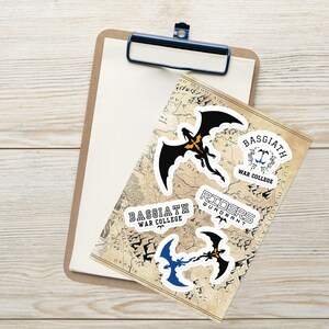 May include: A collection of stickers featuring dragon and text designs. The stickers include a black dragon with gold accents, and text that reads "BASGIATH WAR COLLEGE" and "RIDERS QUADRANT". The stickers are on a map-like background.