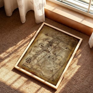 May include: A framed vintage map with a light wood frame. The map displays detailed illustrations of landmasses, a compass rose, and other cartographic elements. The map is resting on a brown carpet, with sunlight streaming in from a nearby window.