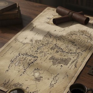 Può includere: Una mappa dettagliata con una rosa dei venti, montagne e testo è appoggiata su una scrivania di legno. Una mappa arrotolata, una lente d'ingrandimento, una tazza di caffè e una candela sono presenti. Tema vintage e fantasy.