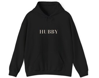 May include: Black hoodie with the word "HUBBY" printed across the chest in a light beige color. The hoodie has a drawstring hood and a front kangaroo pocket. The garment is made of a soft material.