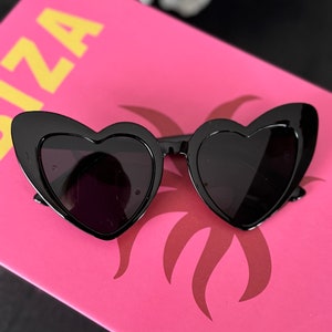 May include: Black heart-shaped sunglasses with a thick frame and dark lenses.