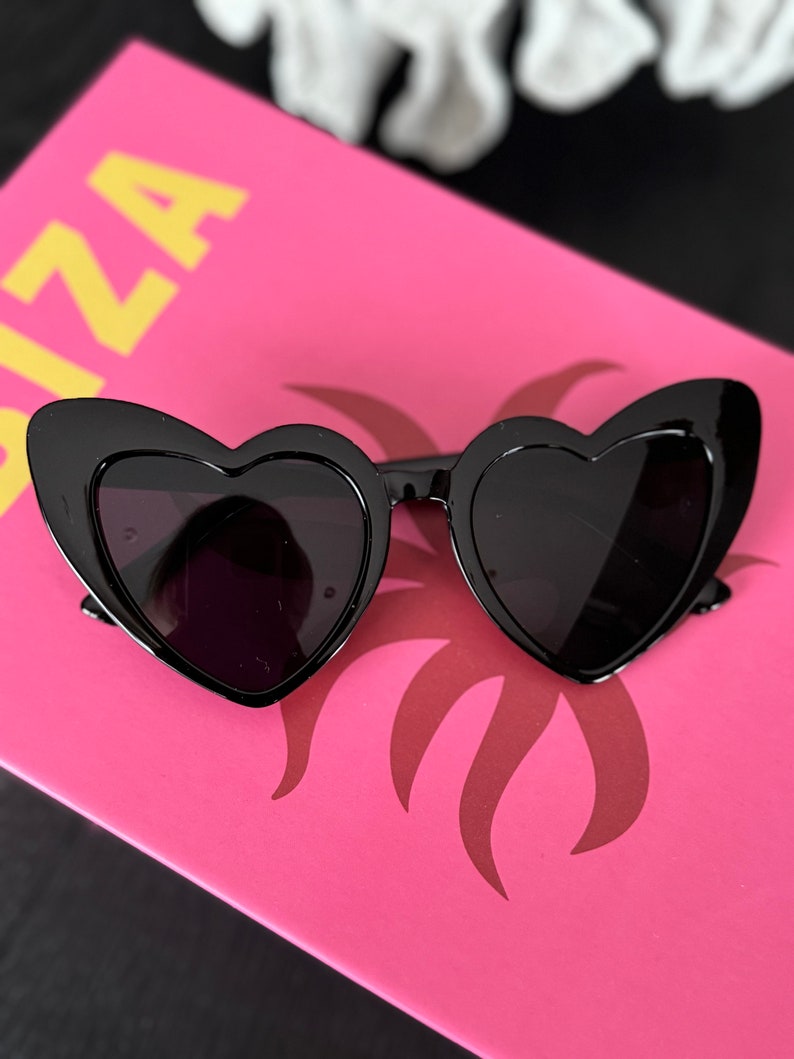 May include: Black heart-shaped sunglasses with a thick frame and dark lenses.