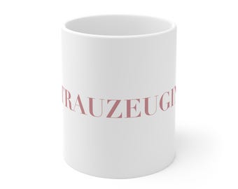 May include: White ceramic mug with the word "Trauzeugen" in pink lettering.