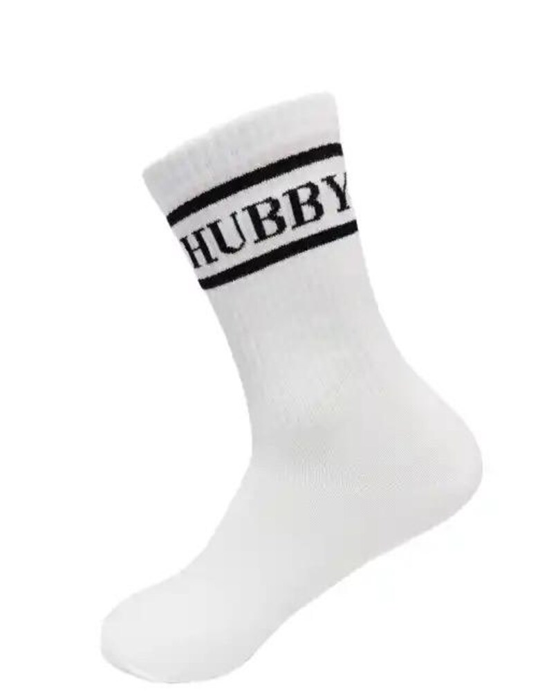 May include: White crew sock with the word "HUBBY" in black block letters. The sock has two black stripes at the top. The sock is made of a soft, comfortable material.