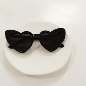 May include: Black heart-shaped sunglasses with a white background.