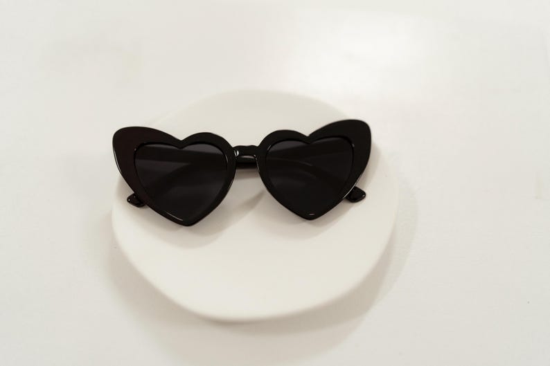 May include: Black heart-shaped sunglasses with a white background.