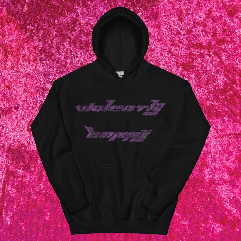 May include: Black hooded sweatshirt with the text "violently happy" in a purple, stylized font. The hoodie has a front pocket and a drawstring hood. The sweatshirt is displayed on a pink textured background.