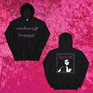 May include: Black hoodie with the words "violently happy" in purple lettering across the chest. The back of the hoodie features a purple framed image of a person. The hoodie is displayed on a pink background.