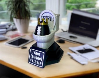 May include: A novelty trophy shaped like a toilet, with a football inside and a crown on top. The toilet has the letters "FFL" on the back. The base of the trophy reads "[Your League] #1 LOSER".