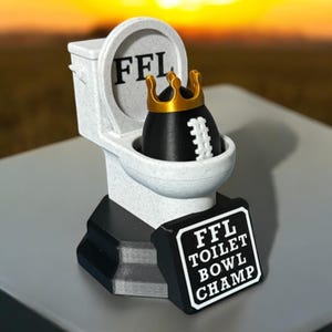 Puede incluir: Un trofeo novedoso que representa un inodoro blanco con las letras "FFL" en la tapa. Dentro del inodoro hay un bal&oacute;n de f&uacute;tbol americano negro con una corona dorada. Un letrero dice "FFL TOILET BOWL CHAMP".