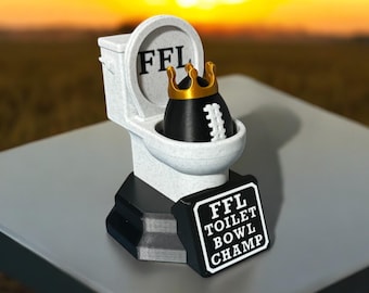May include: A novelty trophy featuring a white toilet with the letters "FFL" on the lid. Inside the toilet is a black football wearing a gold crown. A sign reads "FFL TOILET BOWL CHAMP".