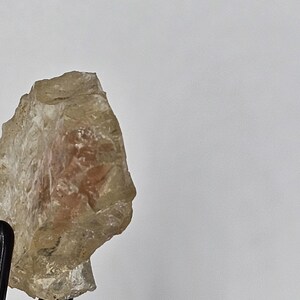 Puede incluir: Un cristal de piedra de sol translúcido, amarillo claro y naranja, con una textura rugosa y natural.