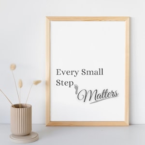 May include: A framed print with the text "Every Small Step Matters" in a modern font. The print is in a light wood frame, and a small vase with dried flowers sits to the left.