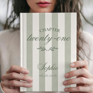 May include: A hardcover book with a vertical sage green and white striped cover. The text reads CHAPTER twenty-one, Sophie, and 06.26.2026, with a small decorative leaf graphic centered between the chapter title and the name.