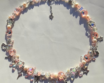 May include: A delicate pink and silver necklace with a variety of charms, including stars, butterflies, and keys. The necklace is made with glass beads and metal accents.
