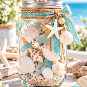 May include: A clear glass mason jar filled with sand, various white and brown seashells, and smooth light blue sea glass. The jar features a silver metal lid, wrapped with natural jute twine and a bright turquoise burlap ribbon bow.
