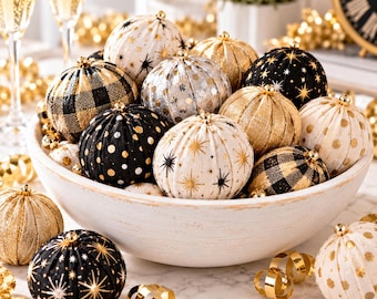May include: A collection of round, fabric-covered ornaments in a white bowl. The ornaments feature black, gold, and white patterns including buffalo plaid, polka dots, and starburst designs, each topped with a small gold-colored cap.