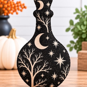 May include: A flat, bottle-shaped fabric ornament featuring a black background with a printed pattern of cream-colored crescent moons, stars, and bare tree silhouettes. The edges are stitched with a visible running stitch detail.
