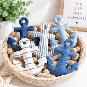 May include: A collection of five fabric anchor ornaments in a wooden bowl filled with wooden spheres. The anchors feature various blue and white patterns, including solid navy, solid light blue, vertical blue stripes, and horizontal blue stripes.