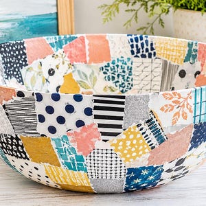May include: A round bowl featuring a colorful patchwork design composed of various square and rectangular segments. The patterns include navy blue polka dots, black and white stripes, mustard yellow, coral pink, and teal geometric prints.