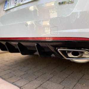 May include: Rear view of a white car with a black rear diffuser and a single chrome exhaust pipe. The car has a red stripe along the bottom of the bumper and a "VRS" badge on the trunk.