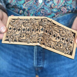 May include: A brown leather wallet with a floral design carved into the surface. The design is in black and the wallet is folded in half.
