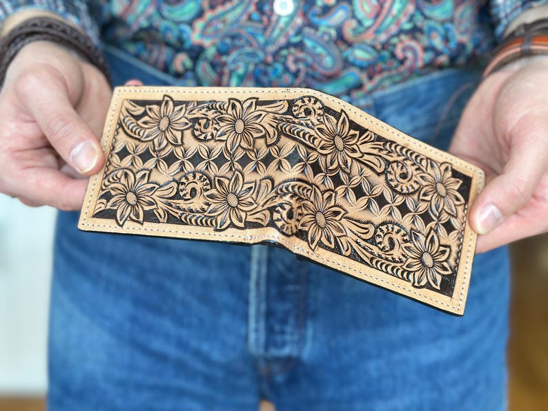 May include: A brown leather wallet with a floral design carved into the surface. The design is in black and the wallet is folded in half.