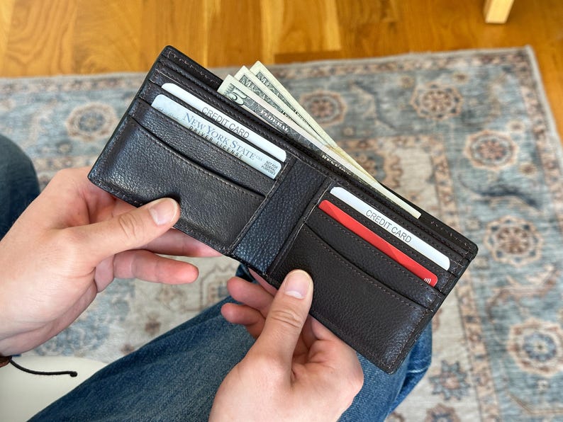 May include: A brown leather wallet open to reveal cash and credit cards. The wallet has two card slots and a cash pocket. The cards are labeled "Credit Card" and "New York State Driver License".