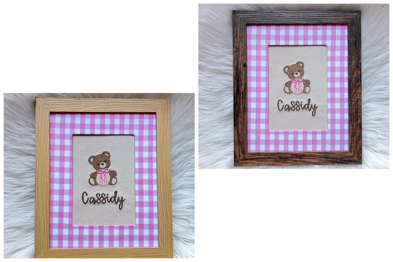 May include: Two framed pictures with a pink and white gingham pattern. Each frame holds a beige rectangle with a brown teddy bear embroidered on it, wearing a pink bow. The name "Cassidy" is embroidered below the bear. One frame is light wood, the other is dark wood.