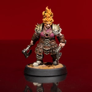 May include: A miniature fantasy figure of a female dwarf warrior with fiery orange hair and a stern expression. She wears brown leather armor, gold shoulder pads, and holds two small axes. The figure stands on a black base against a red background.