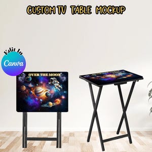 Puede incluir: Dos mesas de TV plegables negras con diseños diferentes. Una mesa tiene un diseño de temática espacial con el texto "Over the Moon". La otra mesa tiene un diseño en blanco y negro.