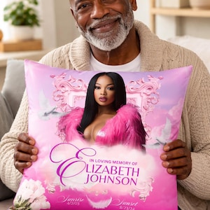 May include: A pink cushion featuring a portrait of a woman in a pink feathered top. The cushion includes the text "In Loving Memory of Elizabeth Johnson" and dates for sunrise and sunset.