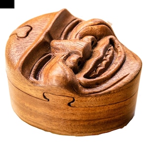 May include: A wooden puzzle box shaped like a smiling face. The box is made of dark brown wood and has a detailed carving of a face with a wide smile and large teeth.