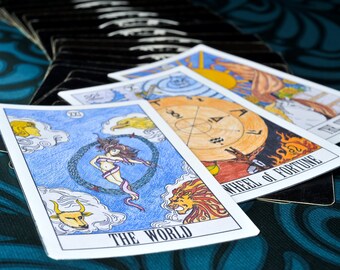 May include: Three tarot cards, The World, Wheel of Fortune, and The Sun, are laid out on a teal patterned surface. The World card features a woman dancing in a circle, a lion, a bull, and an eagle. The Wheel of Fortune card shows a wheel with symbols and a figure in flames. The Sun card depicts a sun with rays and a figure in a white robe.