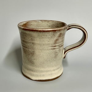May include: A white ceramic mug with a brown rim and handle. The mug has a rustic, handmade look.