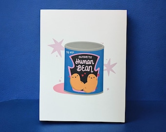 May include: A white card with a blue can illustration that says "Favorite Human Bean". The can has a blue background, a gray lid, and two cartoon beans. Pink starbursts and a pink circle are also on the card.