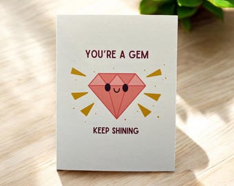 May include: A white card with the text "You're a Gem" and a pink cartoon diamond with a smiling face. The diamond is surrounded by yellow rays of light. The text "Keep Shining" is below the diamond.